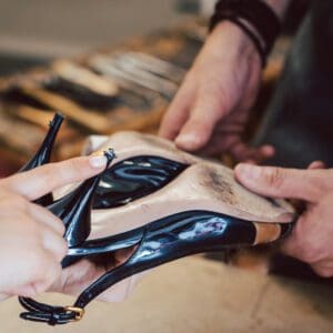 Hand wijst naar een versleten hak op een zwarte pump