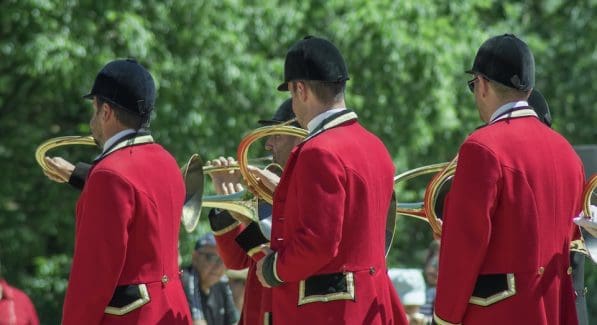 3 mannen in jachtkledij; rode jas, wit hemd en zwarte cap blazend op een jachthoorn.