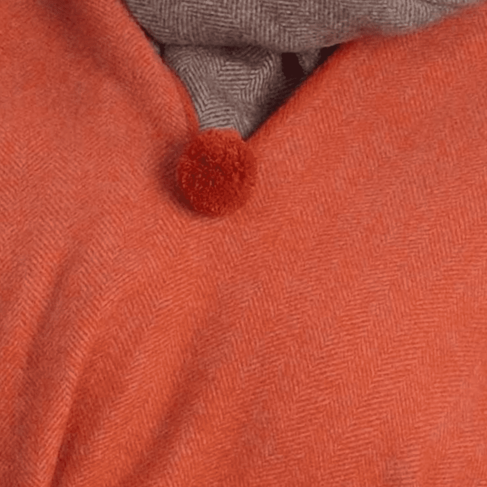 Detail van een oranje poncho met een pompom .
